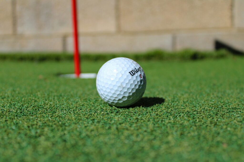 A close-up of a golf ball resting near a red flag on a backyard putting green.